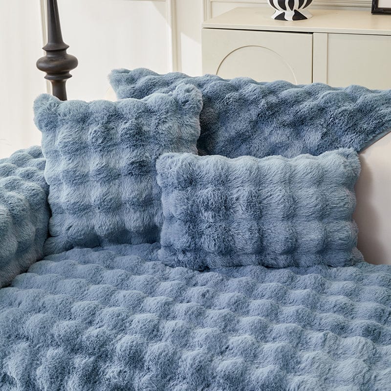 Housse de coussin EasyCover fausse fourrure molletonnée 45×45, à l'unité, Bleu bulles, posée sur un canapé
