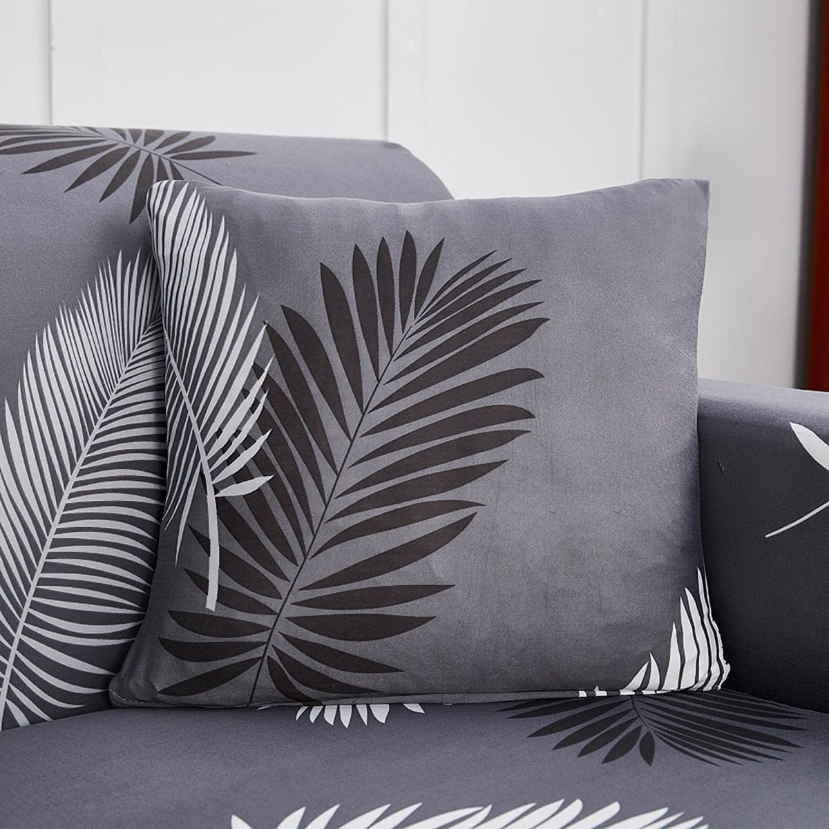 Housse de coussin extensible 45×45, à l'unité, Gris palmes, posée sur un canapé