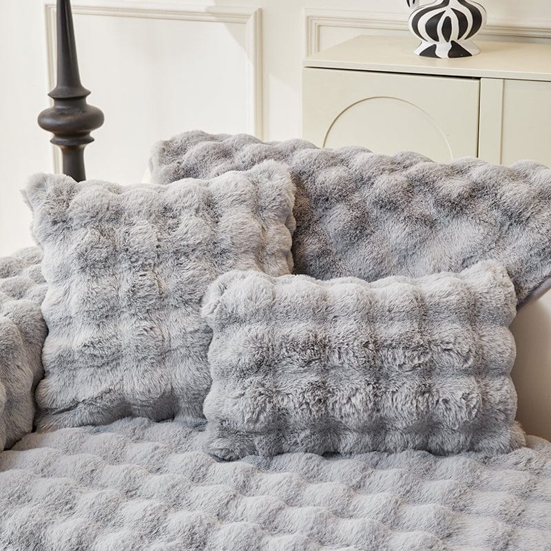 Housse de coussin EasyCover fausse fourrure molletonnée 45×45, à l'unité, Gris perle bulles, posée sur un canapé